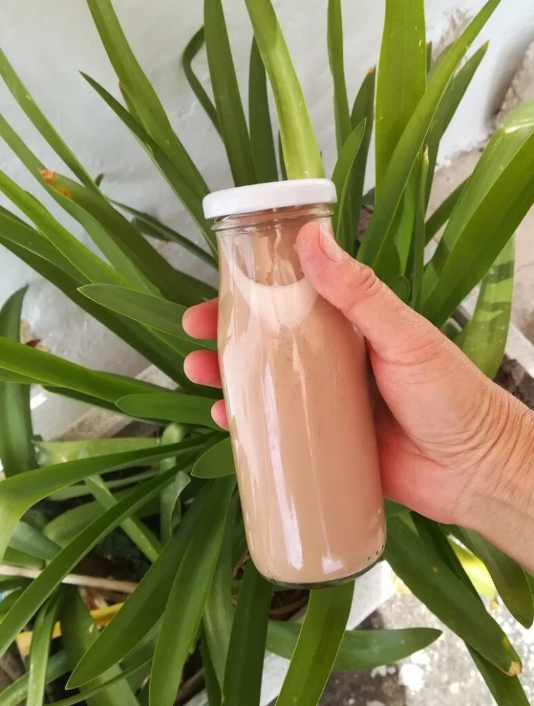 una mano sujeta una botella pequeña de cristal con un batido de chocolate