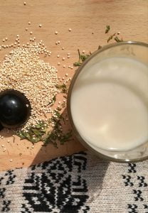 enfocados de arriba a abajo un vaso de leche de quinoa junto a semillas de quinoa y gorro andino