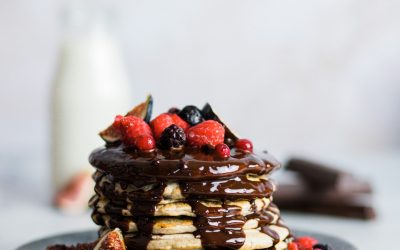 torre hecha con 8 pancakes sobre un plato. Llevan un baño de chocolate y frutas del bosque como topping