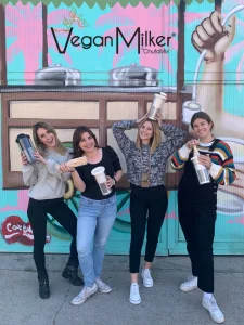 4 trabajadoras de vegan milker posan ante un mural de horchata y cada una muestra un modelo de vegan MIlker