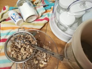 Sobre una mesa yogurtera con yogures rodeado de semillas un bote de almidón y otro de probióticos sobre un trapo de colores