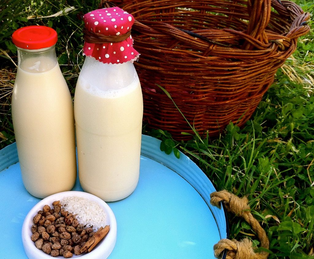 dos botellas de vidrio con leche dentro en una bandeja . Al lado unas semillas y una cesta. 