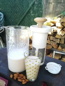 leche de almendras concentrada en un recipiente junto a un vaso de leche y el filtro de vegan milker al fondo
