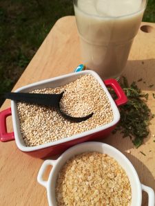 sobre tabla de madera quinoa en grano y quinoa en copos y de fondo un vaso de leche de quinoa