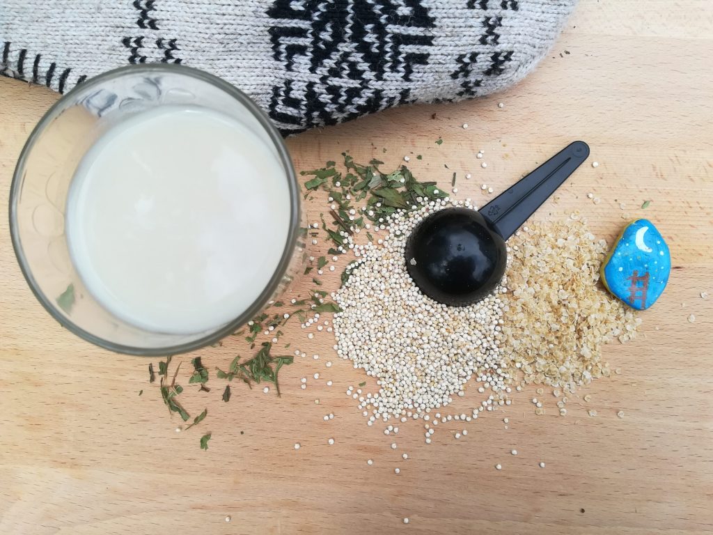 sobre una mesa de madera un vaso de leche de quinoa semillas de quinoa y gorro con motivos andinos