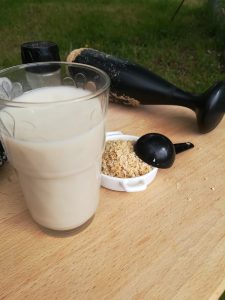 sobre mesa de madera vaso con leche de quinoa y al fondo mortero prensador del utensilio vegan milker con restos de pulpa de quinoa