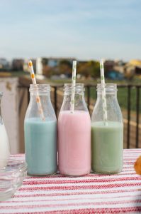tres botellas de cristal con leches de colores sobre mesa