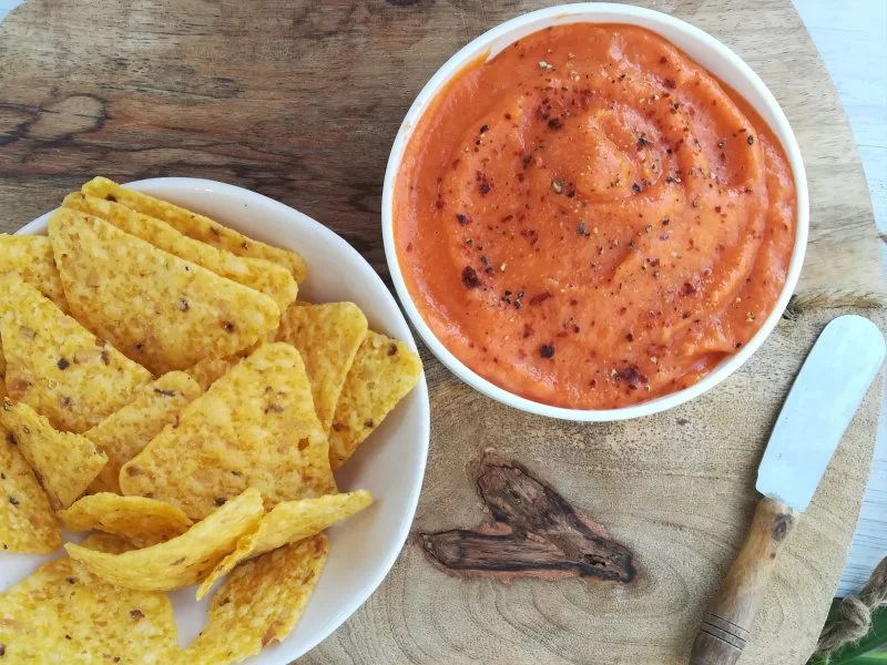 un plato de nachos junto a un cuenco con pure de patata y pimento condimentado con pimienta negra y roja