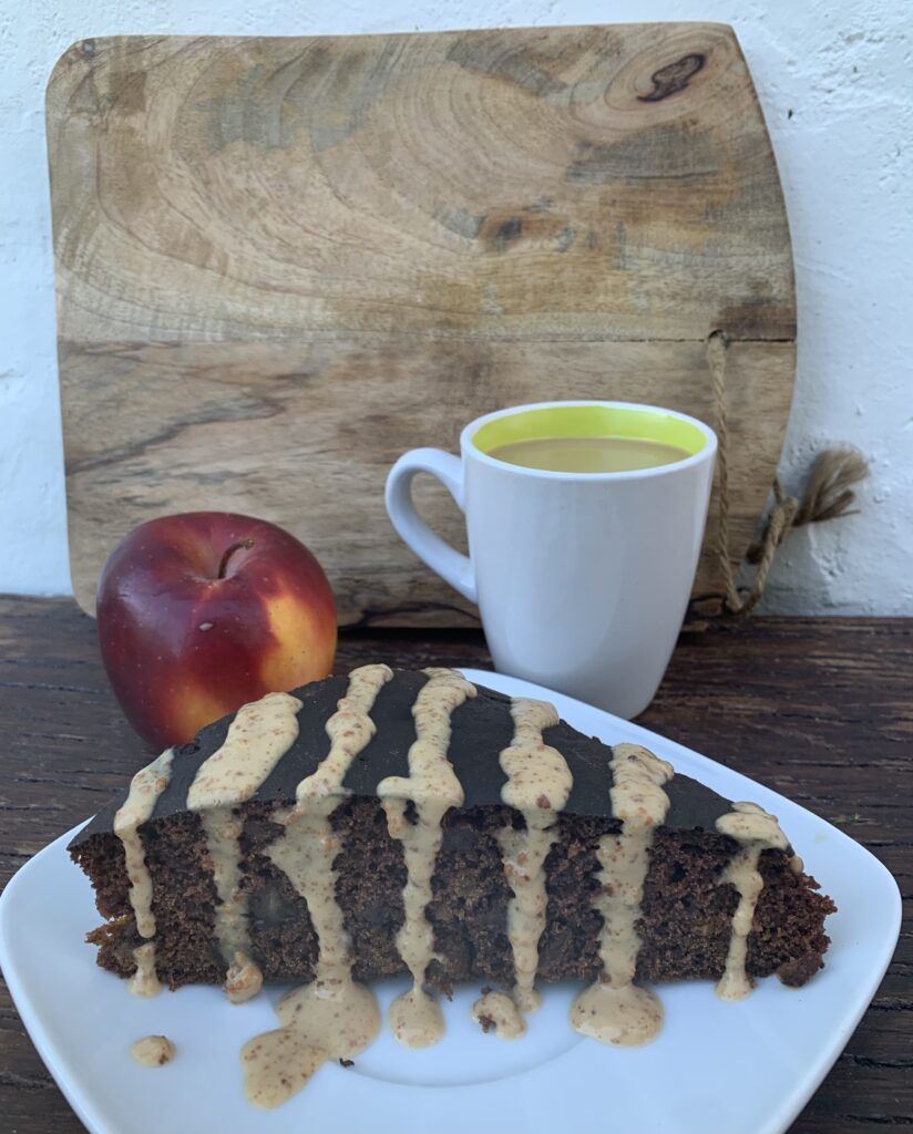 un trozo de bizcocho sobre plato junto a una taza de café y una manzana