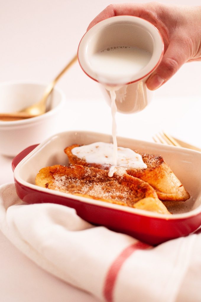 bandeja de cocina con dos torras y una mano con una jarrita de leche vertiendo la leche sobre las torradas