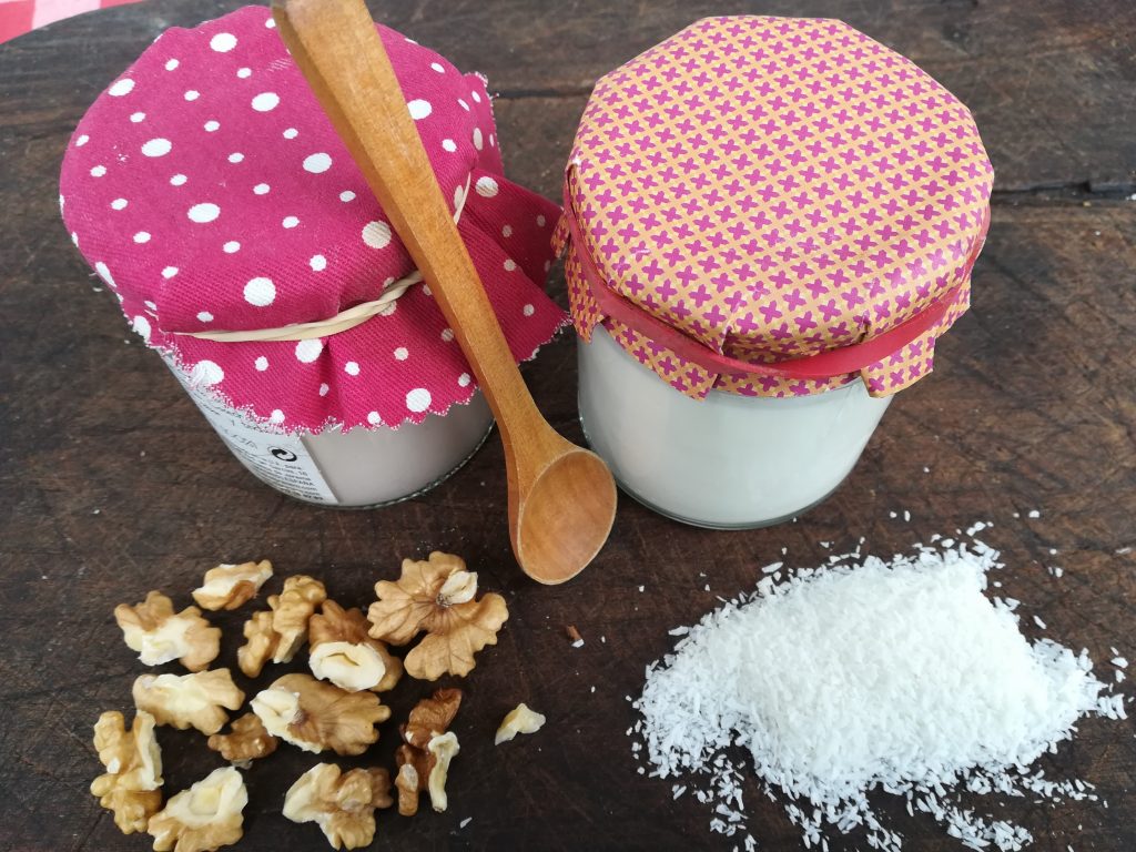 dos tarros de vidrio con yogur sobre la mesa. Coco rayado y nueces al rededor